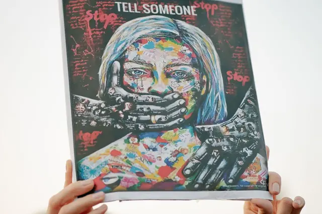一幅示威的标语，图画中的女子被双手掩着嘴巴，印有“Tell Someone”的字眼。