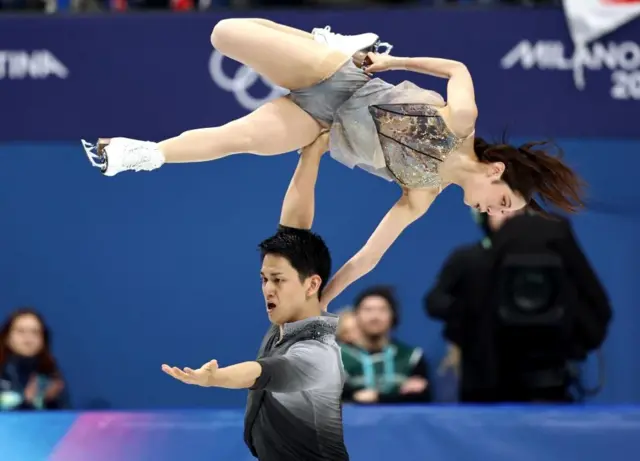 下にいる木原が右手を伸ばして三浦を持ち上げている。三浦は左手を木原の肩にのせ、折り曲げた右脚のスケート靴の刃を右手でつかんでいる