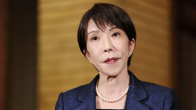 青色っぽいジャケットを着た高市氏が前を見て軽く口を開いている