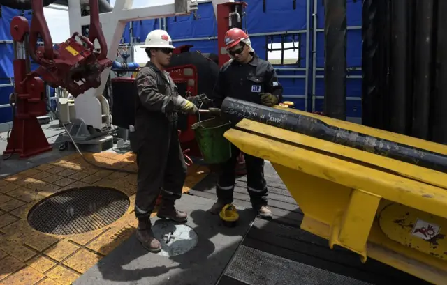 Trabajadores petroleros mirando una tubería.