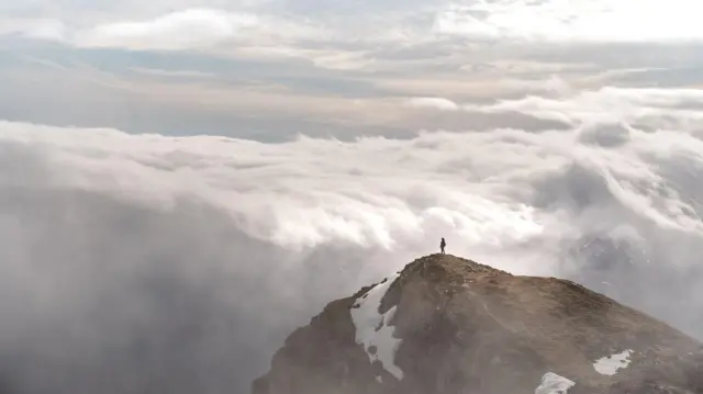 د غره د سر یوه منظره چې یوه ښځه ولاړه ده او ورېځو ته ګوري.