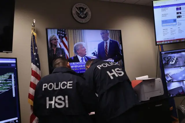 Agentes del DHS frente a un televisor con Donald Trump en la pantalla