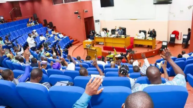 Vue de l'intérieur de l'Assemblée législative de transition avec des membres qui lèvent la main pour voter. 