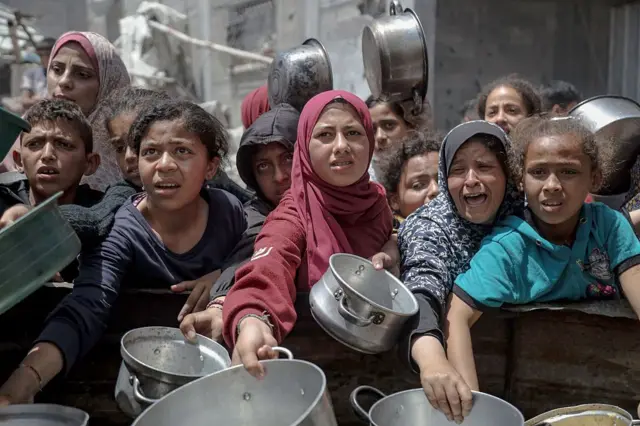 Женщины и дети держат пустые кастрюли, чтобы получить еду в лагере беженцев в Газе на этой неделе