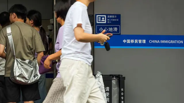 2026年8月1日,廣東省深圳市,人們走進出入境管理服務大廳,一名行人從「中國移民管理」標誌旁經過。