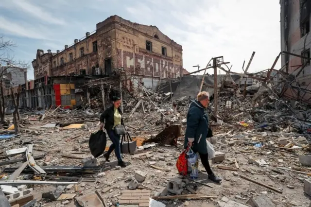 Residents carry their belongings near buildings destroyed in the course of Ukraine-Russia conflict, in the southern port city of Mariupol, Ukraine April 10, 2022.