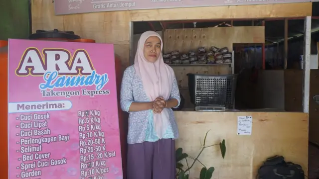 Seorang perempuan berdiri di pinggir poster binatu.