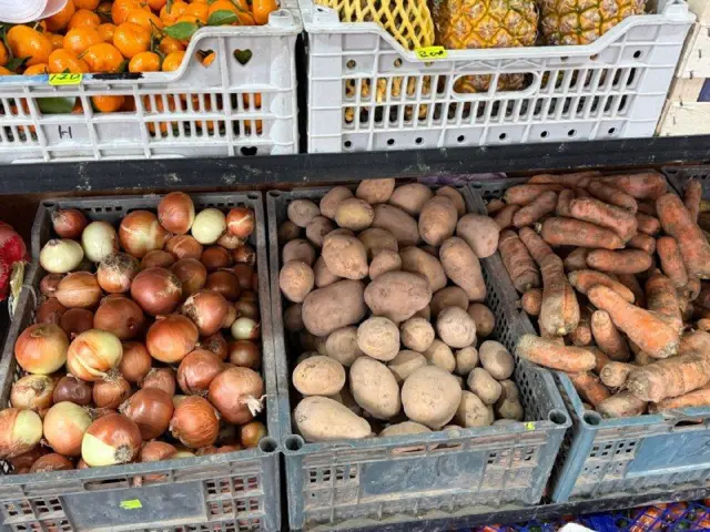 Plastik yashiklarga qolingan piyoz, kartoshka, sabzi. Tepadagi rastada mandarin va ananas bir oz ko'rinib qolgan