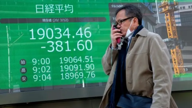 Man walking past stock market board in Tokyo (12 Mar 2020)