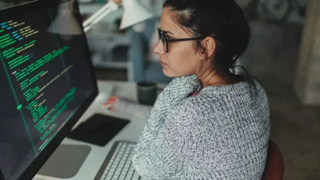 Mujer frente a una computadora manejando lenguaje de código para web.