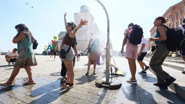 Grupa osób chłodzi się przy zraszaczu na Placu Zamkowym w Warszawie