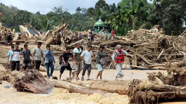 Warga terpaksa melintasi jembatan darurat dari batang kayu akibat jalan dan jembatan penghubung antara Kabupaten Tapanuli Selatan menuju Tapanuli Tengah-Sibolga serta Medan putus diterjang banjir bandang pada Selasa (29/11).