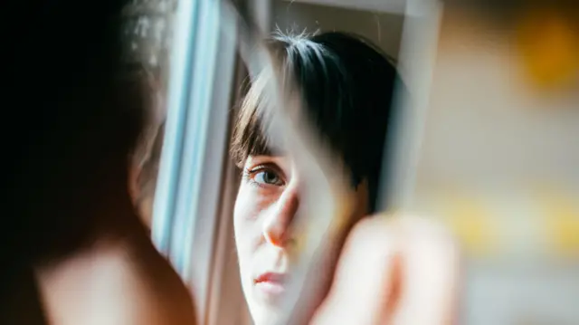 Kırık bir aynaya bakan kadın