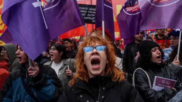 žena viče na protestu u Istanbulu, oko nje ljudi nose ljubičaste zastave 