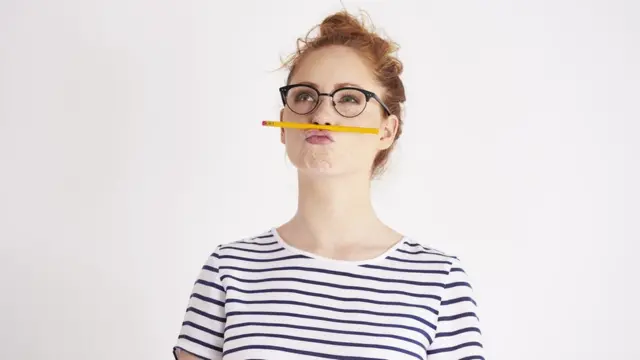 Mujer con un lápiz entre la nariz y la boca.