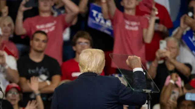 دونالد ترامپ پشت به تصویر برای هوادارانش سخنرانی می‌کند