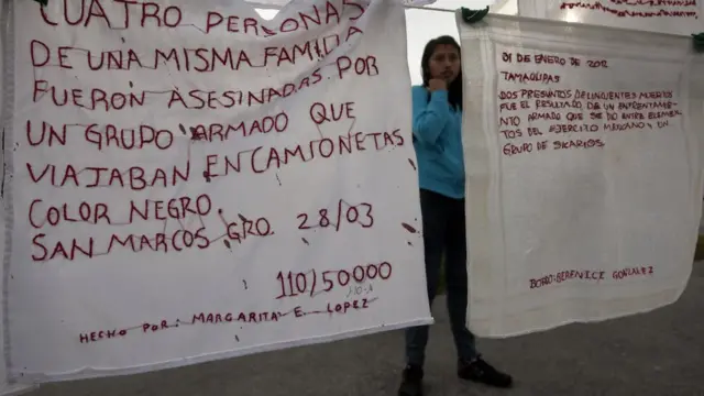 Mujer con mantas en las que se leen mensajes sobre desapariciones y nombres de desaparecidos durante una protesta en Monterrey.