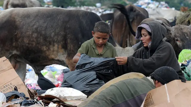 Uma mulher e seu filho procuram comida no lixo