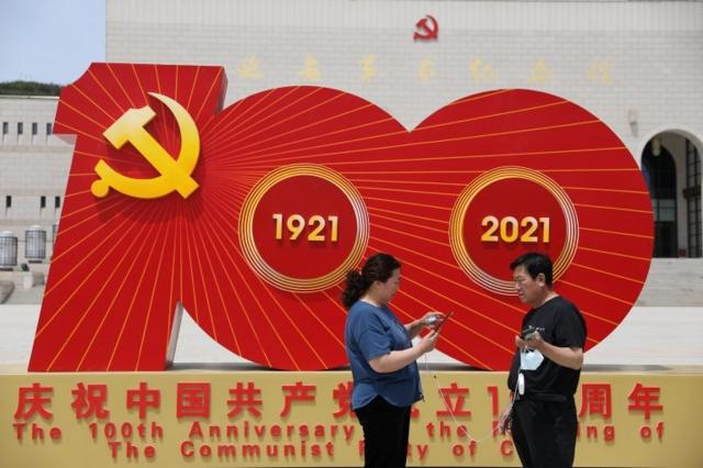คนสองคนยืนหน้าสัญลักษณ์ 100 ปี พรรคคอมมิวนิสต์จีน