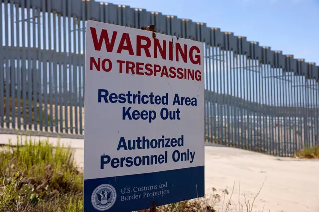 Uma placa da Alfândega e Proteção de Fronteiras dos EUA (CBP) pode ser vista no Parque Estadual Border Field, com o muro da fronteira entre os EUA e o México ao fundo.