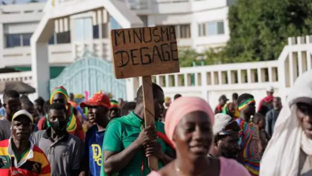 Abaturage bo muri Mali bigaragambya, umwe afite icyapa kiriho ubutumwa busaba ko MINUSMA iva mu gihugu cyabo