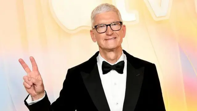 Tim Cook, con corbatín y traje negro, hace la señal de paz con sus dedos.