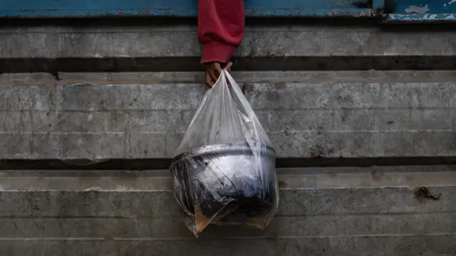 يد فلسطيني نازح يحمل وعاءً في كيس بلاستيكي أثناء وقوفه في الطابور لتلقي الطعام من مطبخ خيري في خان يونس في جنوب قطاع غزة في 11 أبريل/نيسان 2025