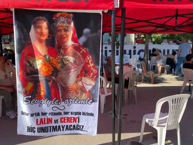 Duruşma salonu dışındaki bekleme alanından bir fotoğraf. Üzerinde "Lalin ve Ceren'i hiç unutmayacağız" yazılı bir pankart gözüküyor.
