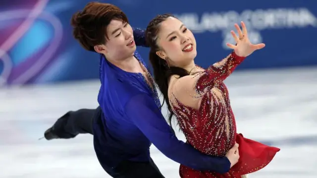 赤い衣装の吉田が左を前に伸ばしている。青と黒の衣装の森田は、後ろから吉田の腰に右手で抱え、左脚を後方に伸ばしている
