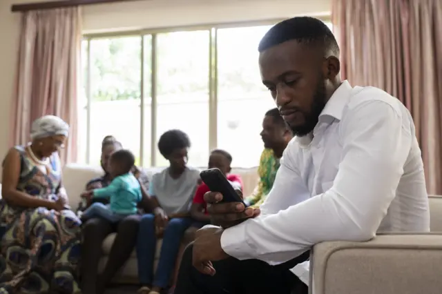 Un homme qui manipule son téléphone en compagnie de sa famille