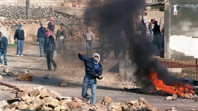 چند فلسطینی با چفیه در حال پراندن سنگ به سوی سربازان اسرائیلی