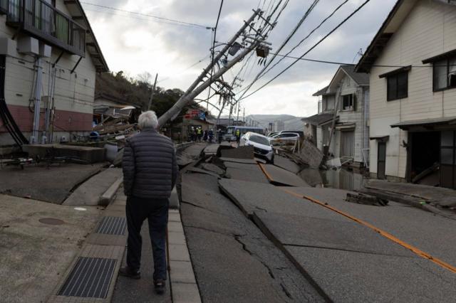 Seorang pria berjalan di sepanjang bagian Rute 249 yang rusak di tengah tiang listrik yang tumbang pada Kamis, 4 Januari 2024 di Kota Wajima, Jepang.