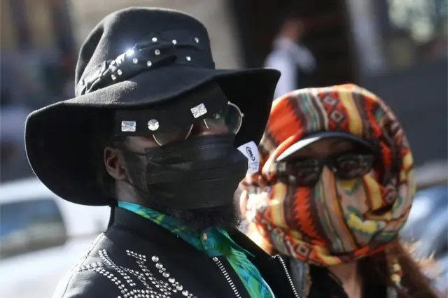 A man and a woman wear sunglasses and improvised masks at Milan Fashion Week.