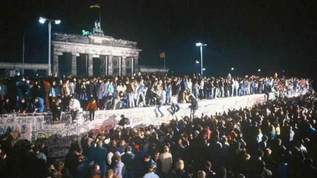 9 November 1989: On this night, 30 years ago, thousands of East Germans rushed to the Berlin Wall and crossed into West Berlin for the first time in almost 30 years. This photo was taken on the night that the border opened and shows people celebrating around the wall. Berlin's famous Brandenburg Gate in the background.