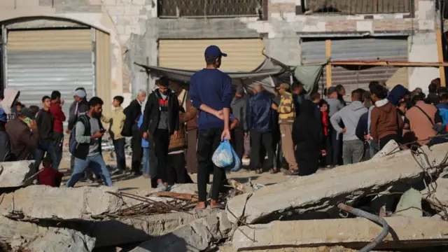 شاب فلسطيني يحمل كيساً بلاستيكياً يحتوي على خبز طازج بينما يصطف آخرون خارج مخبز في مدينة خان يونس جنوب قطاع غزة في 20 نوفمبر/تشرين الثاني 2024