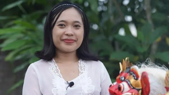 Ni Made Ariyanti yang mengenakan kebaya khas Bali berfoto di depan topeng barong kecil.