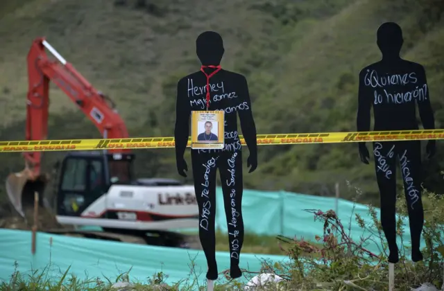 Cartazes com figuras humanas e uma retroescavadeira ao fundo