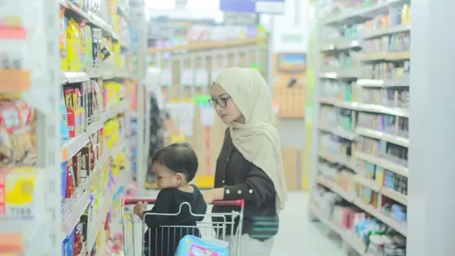 Seorang Ibu muda di Indonesia sedang berbelanja dengan putranya di supermarket atau toko kelontong.