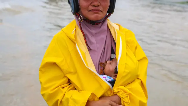 မလေးရှားနိုင်ငံ၊ ကန်ဂါမြို့မှာ မြင့်တက်နေတဲ့ရေကြီးမှုထဲ ကလေးငယ်ကို ရင်ခွင်ပိုက် လမ်းလျှောက်နေတဲ့အမျိုးသမီးတစ်ဦးကို နိုဝင်ဘာလ ၂၇ ရက်တုန်းက မြင်တွေ့ရတာဖြစ်ပါတယ် 