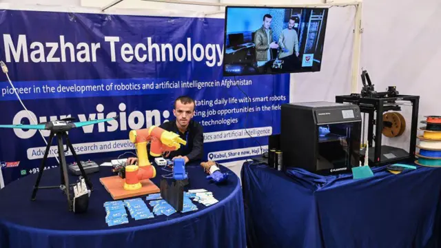 Мужчина сидит за столом, за ним надпись Mazhar Technology, перед ним — визитки, дрон и друга электроника.