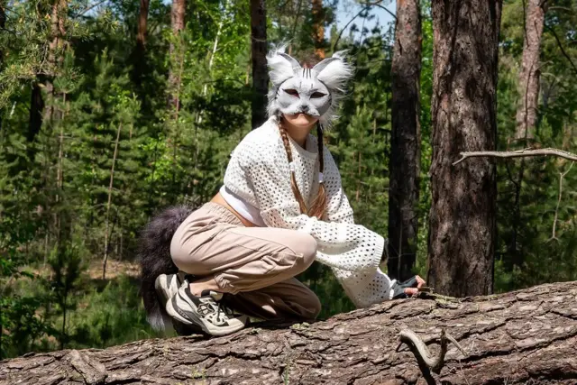 Tinejdžerka nosi masku životinje na glavi i čuči na oborenom drvetu
