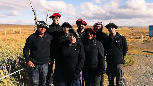 Cecilia Durán Gafo junto a integrantes del equipo de la Reserva Natural Pingüino Rey. Es un grupo de 8 personas. Todas visten de negro y 3 tienen boinas rojas, 4 negras y una de ellas púrpura.