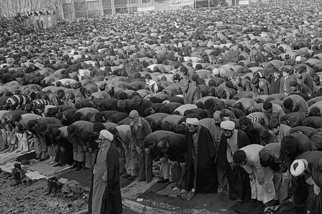 حسین علی منتظری از نزدیکان آیت الله خمینی، نماز جمعه را در دانشگاه تهران اقامه می‌کند. مهدی بازرگان، نخست وزیر سابق، در پشت سر منتظری ایستاده است.