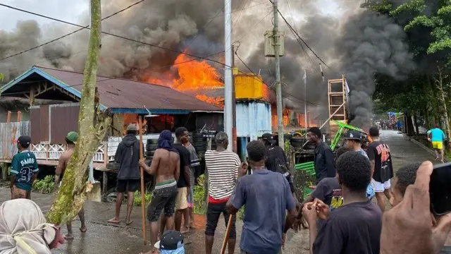 Massa berdiri di depan pos Satgas 123/Rajawali yang terbakar pada Sabtu (28/09) siang.