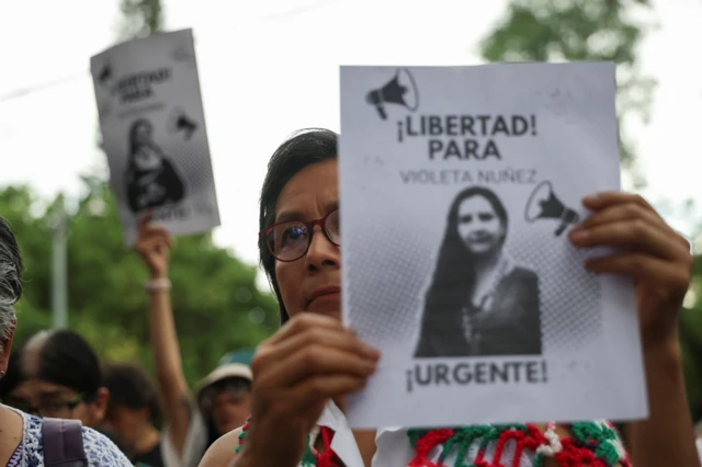 Una mujer con lentes sostiene una pancarta que tiene la foto de una mujer que dice: ¡Libertad para Violeta Núñez, Urgente! 