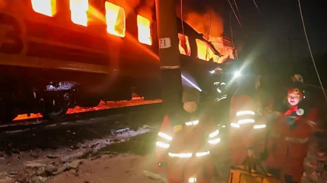 Полыхающий изнутри вагон, рядом стоят спасители, ночь