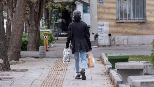 Una mujer camina por la acera llevando bolsas de la compra.
