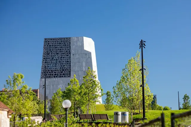 La torre de granito del Centro Presidencial Obama destaca en un frondoso parque verde con bancos y farolas en un barrio de Chicago.