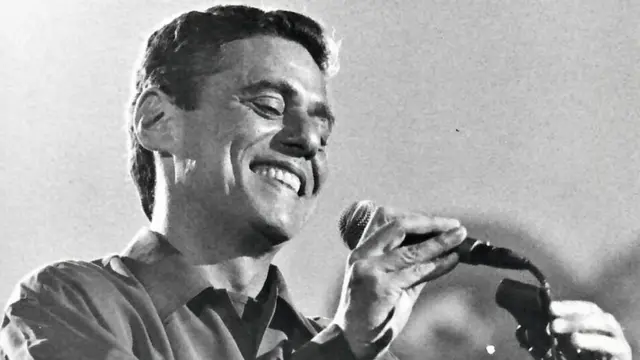 Fotoall in apostas esportivaspreto e branco mostra Chico Buarque sorrindo e tirando microfone do pedestal