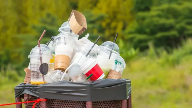 Cubo de basura con vasos de plástico de sitios de comida rápida.
